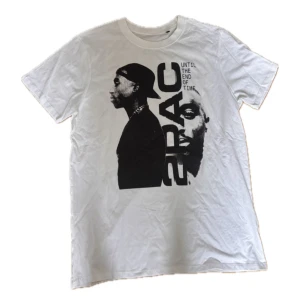 2PAC t-shirt - Vit t-shirt med stort svart tryck av 2PAC och texten 'Until the end of time' på framsidan. Klassisk rund hals och korta ärmar. Materialet är mjuk bomull, perfekt för dig som gillar streetstyle och ikoniska motiv.