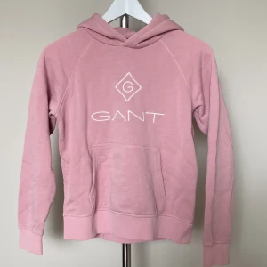 Rosa hoodie från GANT med logga - Säljer en rosa hoodie från GANT med vit broderad logga på bröstet. Tröjan har huva, magficka och långa ärmar. Perfekt för chill dagar och enkel att matcha med jeans eller mjukisbyxor.