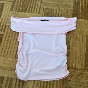 Ljusrosa bandeau tubtopp från SHEIN - Säljer en ljusrosa bandeau tubtopp från SHEIN i storlek S. Toppen är axelbandslös och har rynkade sidor för en snygg passform. Tillverkad i mjuk och stretchig polyesterblandning som känns skön mot huden. Perfekt att styla med jeans eller kjol.