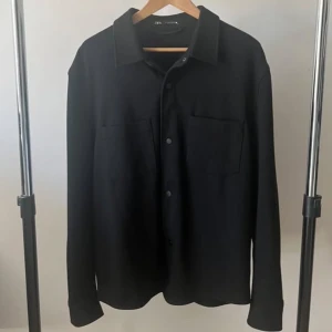 Overshirt Svart  - En helt ny svart overshirt från Zara. 10/10 skick, jag köpte den förra året för 500kr, men jag har använt den 1-2 gånger. Den har inga skador eller liknande. Den är helt ny kan man säga. Väldigt bekväm, man kan ha t shirt under men även hoodie. Det är storlek L, och den sitter även som ett L plagg. Dessa säljs inte mer. Rekommenderar starkt!