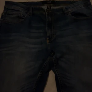 Blå jeans från SMOG, storlek 36/32 - Säljer ett par klassiska blå jeans från SMOG i storlek 36/32. Jeansen har fem fickor, bälteshällor och snygga slitningar framtill. Perfekta till sneakers och hoodie för en chill look.