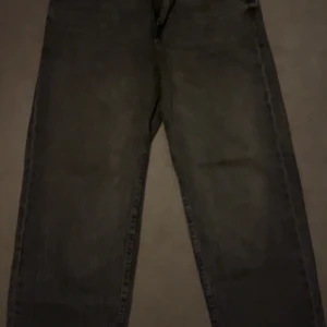 Gråa wide jeans från Bershka - Säljer ett par gråa '90s wide jeans från Bershka. De har en bred passform och klassisk femficksdesign. Jeansen är tillverkade i denim och har en snygg vintagekänsla med raka ben och hög midja. Perfekta för en avslappnad och trendig look.