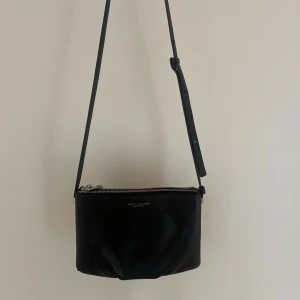 Svart Marc Jacobs väska  - Säljer min axelremsväska från Marc Jacobs i klassisk design 🤍 Väskan är tillverkad i äkta läder med justerbart axelband och silverfärgad dragkedja. Utöver vissa silverdetaljer rostat något är väskan i superbra skick 🌟