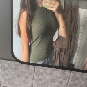 Olivgrön ribbad linnetopp från Object - Säljer en olivgrön ribbad linnetopp från Object i storlek S. Toppen är ärmlös med hög hals och har en tight passform som framhäver figuren. Perfekt till sommaren och enkel att matcha med jeans eller kjol.