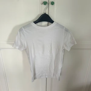 Vit basic t-shirt från H&M - En klassisk vit t-shirt från H&M i mjuk bomull. Modellen är enkel med rund hals och korta ärmar, perfekt att matcha med jeans eller shorts. Snygg och stilren för en clean look.