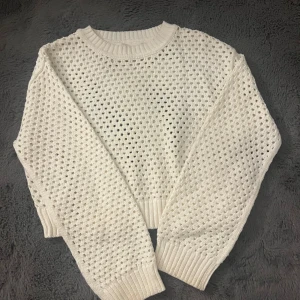 Vit stickad tröja med hålmönster - Vit stickad tröja med hålmönster och ribbade muddar vid ärmslut, hals och nederkant. Tröjan har en loose passform och är långärmad, perfekt för lager-på-lager och en chill vibe.