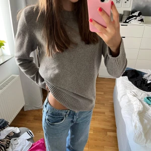 Grå stickad tröja med rund hals - Mysig grå stickad tröja med rund halsringning och ribbade muddar vid ärmslut och nederkant. Perfekt att slänga på sig när det är kyligt ute. Passar till jeans eller kjol för en avslappnad look.