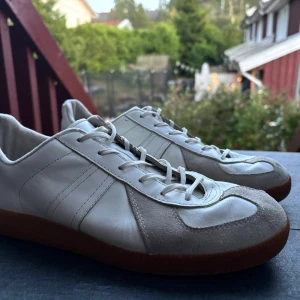 Vintage German Army Trainers (GATS) - Säljer ett par stilrena vita sneakers med grå mockadetaljer och klassisk brun gummisula. Skorna har snörning och en låg profil, perfekt för dig som gillar minimalistisk och clean stil. Materialet är en mix av skinn och mocka för en snygg kontrast.