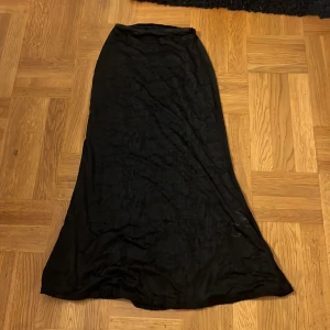 Svart långkjol med diskret mönster - Säljer en svart långkjol med subtilt blommönster i tyget. Kjolen har en rak och något utsvängd passform som ger en snygg siluett. Perfekt för dig som gillar stilrena och eleganta plagg med en twist. Från Gina tricot i storlek xs köpt för 459