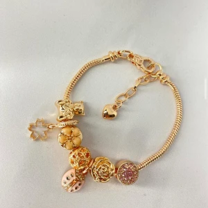 Guldigt charmarmband med berlocker - Superfint armband i guldton med flera detaljerade berlocker som blomma, nalle, hjärta och en söt nyckelpiga. Några berlocker är glittriga och andra har blommönster. Ej använd utan kommer från min small business. 