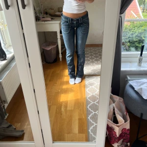 Blå pepejeans bootcut jeans med detaljer - Säljer ett par snygga blå jeans från pepe jeans med bootcut passform och låg midja. Jeansen har coola sömdetaljer på fickorna och slitningar på ena benet för en trendig look. Perfekta om du gillar jeans med lite edge och markerade fickor.