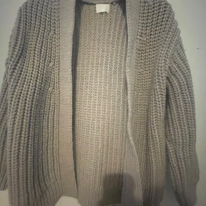 Beige stickad kofta med grov struktur - Mysig beige stickad kofta med grov struktur och öppen framtill. Koftan har långa ärmar och breda ribbade muddar vid ärmslut och nederkant. Perfekt att slänga på sig när det är kyligt ute. Kofta från hm 