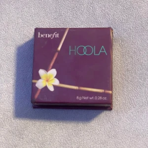 Benefit Hoola Bronzer 8g - Säljer en klassisk Hoola bronzer från Benefit i originalförpackning med spegel. Färgen är matt och varm brun, perfekt för contouring eller solkysst look. Kommer i en snygg lila box med tropisk design och blomdetalj. Innehåller 8g puder. Använt fåtal gånger. Säljer då jag rensar ut smink och den ej kommit till användning på senaste. Pris kan diskuteras💞