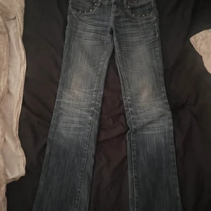 Blå bootcut low waisted flared jeans med nitar från Yishion - Snygga blå bootcut jeans från Yishion med slitningar och coola nitar på framfickorna. Bakfickorna har broderade detaljer och pärlor som ger extra edge. Jeansen har låg midja och klassisk femficksdesign. Perfekta för dig som gillar en unik och trendig look.