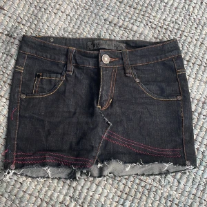 Svart jeanskjol från Gina Tricot - Mörk jeanskjol från Gina Tricot med  coola rosa sömmar framtill. Köpt secondhand och har sytt om, har själv inte andvänt. Storlek 25 men för stor för mig som är 1,65 så stor i storleken