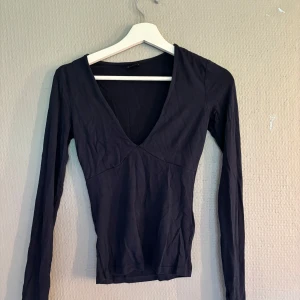 Svart långärmad topp från Gina Tricot - En svart långärmad topp från Gina Tricot i storlek XS. Toppen har djup v-ringning och är figurnära i modellen. Perfekt att styla med jeans eller kjol för en snygg look.