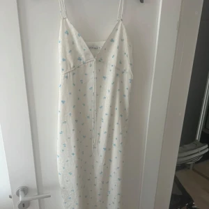 Vit långklänning med blå blommor från Adoore - Supersöt maxiklänning från Adoore i vit nyans med små blå blommor.Klänningen har smala axelband, v-ringning och en luftigare passform! Justerbart band i ryggen Och under bysten som gör att man kan välja så det blir Perfekt passform. Köpte den med prislapp i somras på vinted och använde den under midsommar endast. Såg att det blivit små ”rispor” som jag antar beror på att den suttit för tight på mig när jag gått i den. Men dessa syns knappt! Nypris 1500 ca