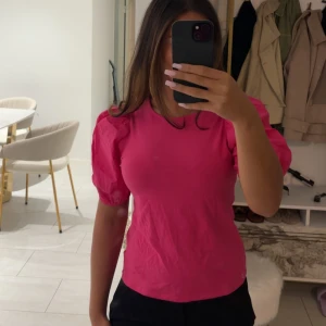 Rosa puffärm blus från H&M - Superfin rosa blus från H&M med puffiga korta ärmar och rund halsringning. Toppens material känns mjukt och lätt, perfekt för att ge en färgklick till din outfit. Enkel och stilren design som ändå sticker ut med sina voluminösa ärmar.
