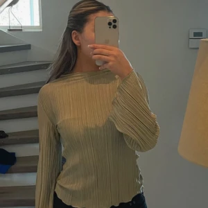 Beige ribbad blus från Stockh LM Studio - Säljer en beige ribbad blus från MQ i storlek XS. Toppen har långärmade, lätt utsvängda ärmar och en cool plisserad struktur. Materialet är glansigt och känns lyxigt, med vågig kant vid hals och nederdel. Perfekt för dig som gillar stilrena detaljer.