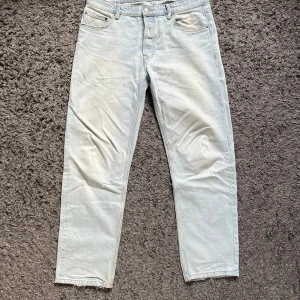 Ljusblå raka jeans med rå kant - Säljer ett par ljusblå jeans med rak passform och klassisk femficksdesign. Jeansen har en snygg, rå kant nertill och är tillverkade i bomull. Perfekta för en avslappnad och trendig look.