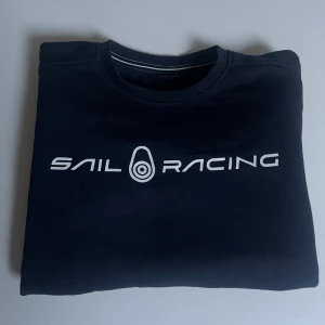 Mörkblå Sail Racing sweatshirt - Mörkblå sweatshirt från Sail Racing med vit logga tryckt över bröstet. Klassisk rund halsringning och ribbade muddar vid ärmslut och nederkant. Bra passform vid rätt storlek✅