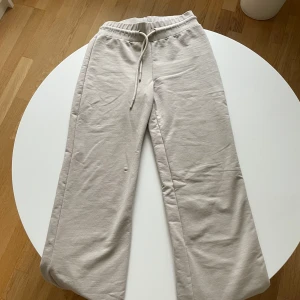 Beige mjukisbyxor från 157 XS - Beiga mjukisbyxor från 157 i storlek XS. Byxorna har resår och snörning i midjan för skön passform. Tillverkade i mjukt bomullsmaterial och har raka ben. Perfekta för chill dagar eller när du vill vara extra bekväm.