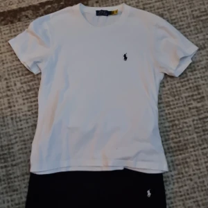 Vit t-shirt från Polo Ralph Lauren - Vit t-shirt från Polo Ralph Lauren med klassisk rund hals och korta ärmar. T-shirten har den ikoniska broderade loggan i marinblått på bröstet. Tillverkad i mjuk bomull för skön passform och clean look.