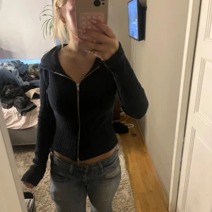 mörkblå zip hoodie från Gina Tricot - mörkblå zip hoodie från Gina Tricot i figurnära modell. Tröjan har dragkedja framtill, huva och långa ärmar. Perfekt för dig som gillar en enkel men snygg look. Passar till jeans eller kjol för en chill vibe.