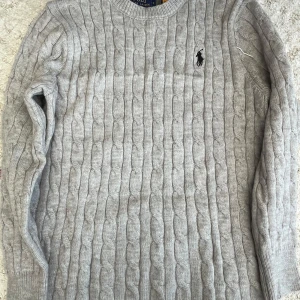 Grå kabelstickad tröja Polo Ralph Lauren - Säljer en grå kabelstickad tröja från Polo Ralph Lauren i storlek S. Tröjan har rund hals, lång ärm och den klassiska broderade loggan på bröstet. Perfekt för dig som gillar stilrena och tidlösa plagg med snygg struktur. Materialet är mjukt och skönt. Kan passa XS i vissa fall