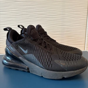 Nike Air Max 270 helsvarta sneakers - Nike Air Max 270 sneakers i helsvart med ventilerande mesh-ovandel, synlig Air-enhet i hälen och diskreta loggor. Snygg sportig look med snörning och rund tå. Perfekta för dig som gillar streetstyle och komfort. Sparsamt använda .Kvitto från inköp i maj 2025