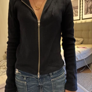 Svart ribbad hoodie från Gina Tricot - Svart ribbad hoodie från Gina Tricot i storlek M. Tröjan har dragkedja framtill, huva och är långärmad. Perfekt för dig som gillar en enkel men snygg look. Passformen är normal och materialet känns mjukt och bekvämt.