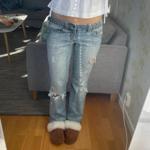 Lågmidjade ljusblå slitna jeans från guess - !INTRESSEKOLL!tryck ej på köp nu,  Säljer ett par lågmidjade ljusblå jeans med slitningar och hål på knäna. Jeansen har klassisk femficksdesign, raka ben och en flätad detalj i midjan. Perfekta för dig som gillar en avslappnad och trendig look.