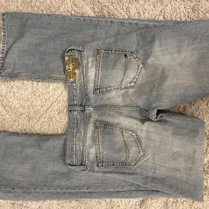 Lågmidjade bootcut jeans  - Säljer ett par ljusblå jeans från Tommy Hilfiger med bootcut-modell. Jeansen har klassiska fem fickor, diskret logga på myntfickan och etikett bak i midjan. De är tillverkade i bomull och har en utsvängd passform nertill och Lågmidjade. W29 och L34