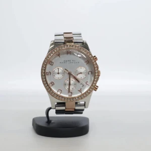 Marc by Marc Jacobs silver/guld klocka - Stilren klocka från Marc by Marc Jacobs med rund urtavla i silver och detaljer i roséguld. Urtavlan har tre små visare och glittrande stenar runt boetten. Länken är tvåfärgad i silver och roséguld, vilket ger en lyxig känsla. Perfekt accessoar för att lyfta din outfit.          Behöver ett nytt batteri.