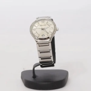 Silverfärgad klocka från Facit - Stilren klocka från Facit i silverfärg med metallarmband och rund urtavla. Urtavlan har diskreta ränder, tydliga siffror och datumvisning vid klockan 6. Ringen runt urtavlan är dekorerad med små stenar för extra bling.                                                                                   Behöver ett nytt batteri.