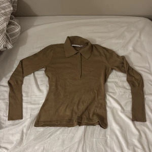 Beige stickad pikétröja med krage - Snygg beige stickad pikétröja med klassisk krage och lång ärm. Tröjan har en smal passform och ribbade muddar vid ärmslut och nederkant. Perfekt för dig som gillar en stilren och enkel look. Tröjan är en ridtröja köpt från PS of Sweden