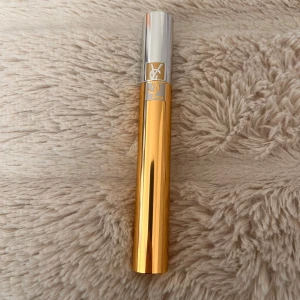 YSL Volume Effet Faux Cils Mascara - Lyxig mascara från Yves Saint Laurent i färgen 01 Black. Kommer i en snygg guldfärgad tub med silverlock och YSL-logga. Ger volym och intensitet till fransarna för en dramatisk look. Perfekt för dig som vill ha fylliga och svarta fransar.