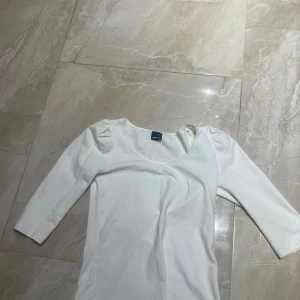 Vit topp med puffärm från Gina Tricot - Säljer en stilren vit topp från Gina Tricot med rund halsringning och diskreta puffärmar. Toppen har trekvartsärm och är gjord i mjuk bomull, perfekt för en clean och enkel look.