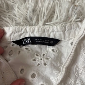 Vit broderad blus från Zara - Superfin vit blus från Zara med broderade blommor och hålmönster. Blusen har v-ringning och långa ärmar, perfekt för en fräsch och romantisk look. Tillverkad i bomull som känns mjuk mot huden och passar perfekt till jeans eller kjol.