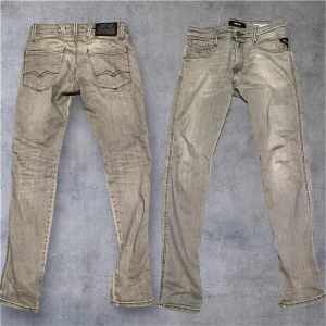 Replay Anbass grå jeans - Snygga grå jeans från Replay, modell Anbass med slim fit. Klassisk femficksdesign, svarta kontrastsömmar och diskret Replay-logga på bakfickan. Jeansen är i stretchigt denim för en bekväm passform och har dragkedjegylf.