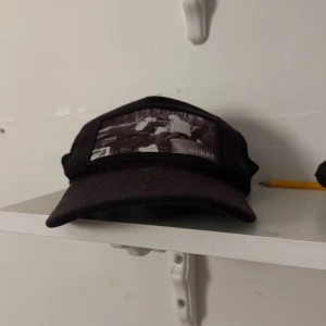 limited edition Gukki Clothing keps - Svart keps med böjd skärm och mesh på sidorna för extra ventilation. Framtill finns en svartvit patch med motiv av personer som chillar på soffor och texten 'GUKKI'. Justerbar baktill för perfekt passform. Snygg och streetinspirerad stil.