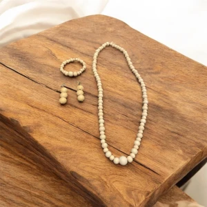 Set med halsband, armband och örhängen i beige pärlor - Elegant set med halsband, armband och örhängen gjorda av beige pärlor. Halsbandet är långt och klassiskt, medan armbandet är elastiskt för enkel passform. Örhängena har en stilren design med tre lite större pärlor. Perfekt för att komplettera en stilren look.