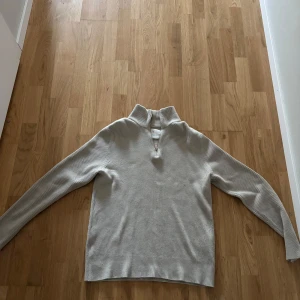 Beige ribbad tröja från Jack & Jones - Säljer en stilren beige ribbad tröja från Jack & Jones. Tröjan har en dragkedja vid halsen och långa ärmar, perfekt för kyligare dagar. Den är både bekväm och snygg, idealisk för en avslappnad look.