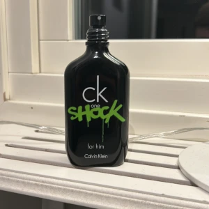 CK One Shock for Him - Säljer en flaska CK One Shock for Him från Calvin Klein. Flaskan är svart med en cool grön textdesign. Perfekt för den som gillar en fräsch och ungdomlig doft. Flaskan har en modern och stilren form som passar perfekt i badrumshyllan.