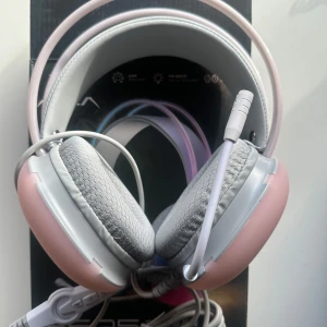 Rosa och grå gaming headset - Snyggt gaming headset i rosa och grått med vadderade öronkuddar för extra komfort. Perfekt för långa spelsessioner med justerbar mikrofon och flexibel huvudbygel. Ansluts enkelt via kabel. Lyser vid användning. 