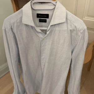 Ljusblå skjorta från Massimo Dutti - Snygg ljusblå skjorta från Massimo Dutti i ett klassiskt snitt. Skjortan har långa ärmar och knappar framtill. Perfekt för en stilren look.