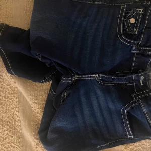 Mörkblå jeans med kontrastsömmar - Snygga mörkblå jeans med vita kontrastsömmar och klassisk femficksdesign. Byxorna har en bootcut-stil som ger en retro känsla. Perfekta för en avslappnad look. Det är en barnstorlek , stl 164. Men passar äldre vid stl xs,s och även M. Pris kan även diskuteras vid intresserad köp. 