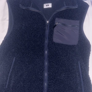 Mörkblå fleeceväst med dragkedja - Säljer en mörkblå fleeceväst med dragkedja och praktisk bröstficka med dragkedja. Perfekt för lager-på-lager under kyliga dagar. Västen har en stilren design och är lätt att matcha med andra plagg.