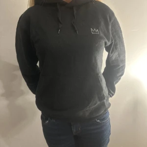 Hov1 hoddie - Snygg svart hoodie med en liten krona på framsidan och ett stort turnétryck på baksidan. Perfekt för dig som gillar att visa upp din musiksmak. Den har en klassisk passform med långa ärmar och en praktisk ficka framtill.