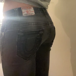 Svarta jeans från True Religion - Snygga svarta jeans från True Religion med klassisk femficksdesign och knappgylf. Jeansen har en tight passform och är perfekta för en stilren look. Märkets ikoniska logga syns på bakfickan.